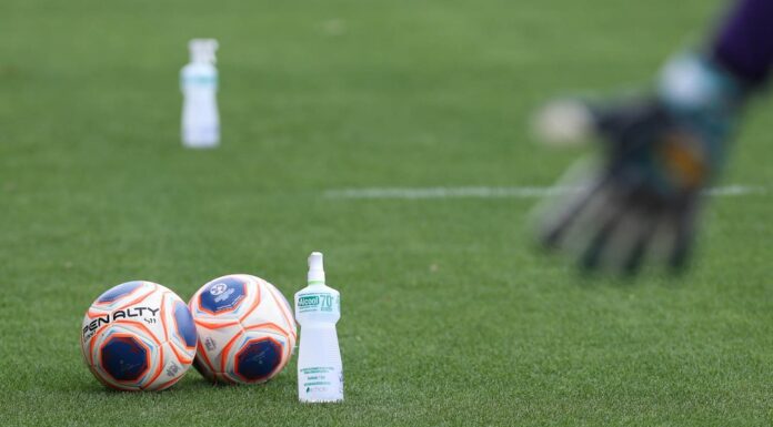 Bolas de futebol no gramado com um frasco de álcool gel.
